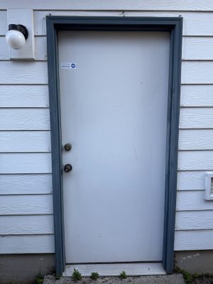 A closed white door with blue-gray frame, two knobs, and a light outside; painted exterior by Pearl Painters in Portland.