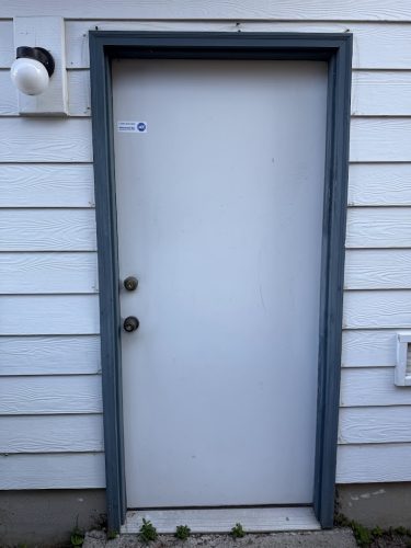 A closed white door with blue-gray frame, two knobs, and a light outside; painted exterior by Pearl Painters in Portland.