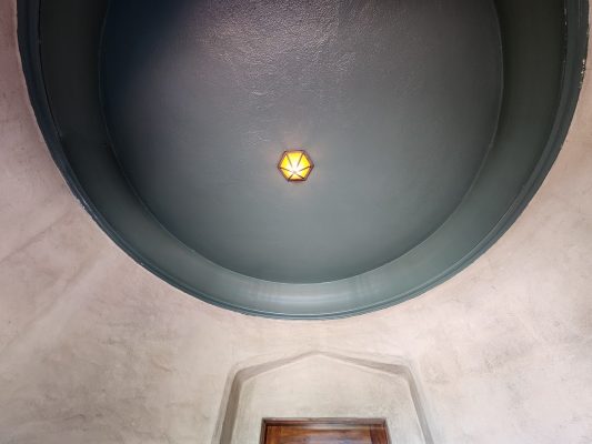 A geometric light fixture hangs on a dark dome ceiling above a doorway with textured plaster walls, painted by Pearl Painters in Portland.