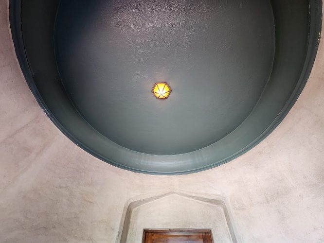 A geometric light fixture hangs on a dark dome ceiling above a doorway with textured plaster walls, painted by Pearl Painters in Portland.