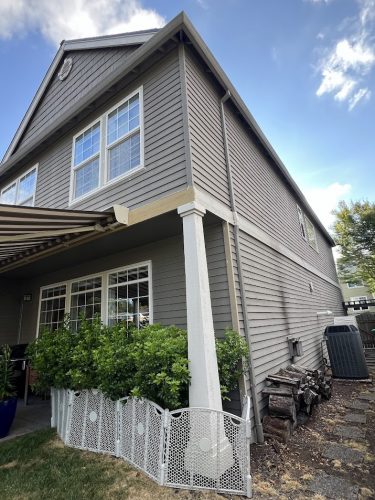 Portland painter's view: two-story Feldon house, gray siding, white trim; Pearl Painters painting; patio; shrubs; firewood.
