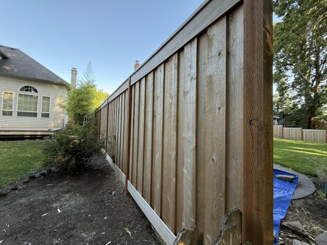 A new wooden fence divides two yards at the Smiths’ home. House and trees behind, clear July 2025 sky. Painted by Pearl Painters.