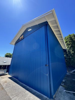 Blue wooden shed with white roof and concrete pavement, painted by Pearl Painters in Portland on a sunny July 2025 day.