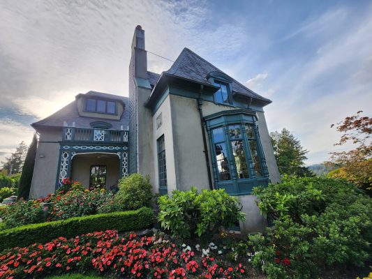 Painting of a two-story house with blue-trimmed windows, green shrubs, red flowers; Ralph Barron style. Pearl Painters, Portland.