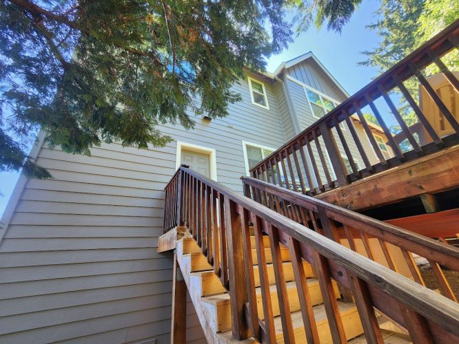 Gray two-story Holley house with wooden stairs and railing, partially shaded by trees, painted by Pearl Painters in Portland.
