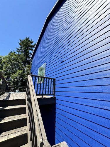 Wooden stairs to a deck next to a blue building in Jennings, with trees and sky; painting by Pearl Painters.