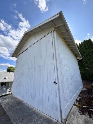 White wooden shed by Deppe on concrete pad under partly cloudy sky, painted by Pearl Painters in Portland.