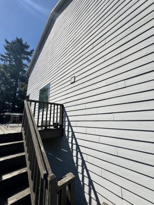 Pearl Painters painting a wooden outdoor staircase and deck on a white-sided building in Jennings, trees and sky in background.