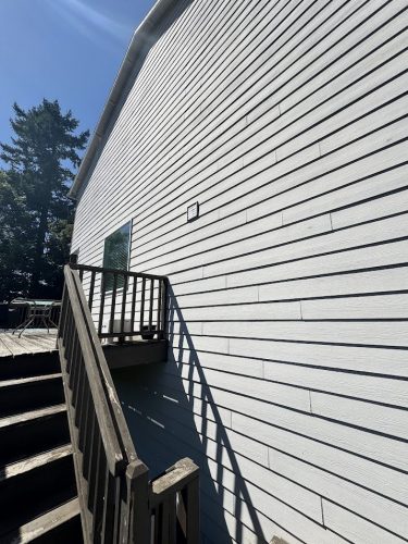 Pearl Painters painting a wooden outdoor staircase and deck on a white-sided building in Jennings, trees and sky in background.