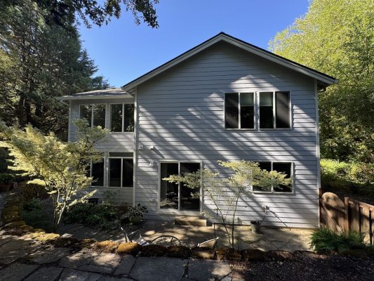 A painter finished a two-story light gray Anderson house with large windows and stone patio, painted by Pearl Painters in Portland.