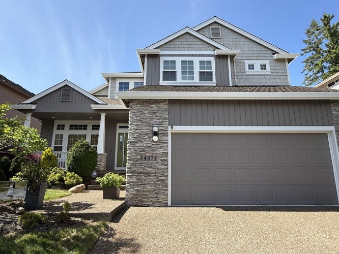 Two-story suburban house in Portland with gray siding, stone accents, and a double garage painted by Pearl Painters. Part of the Hendricks collection, available May 2025.
