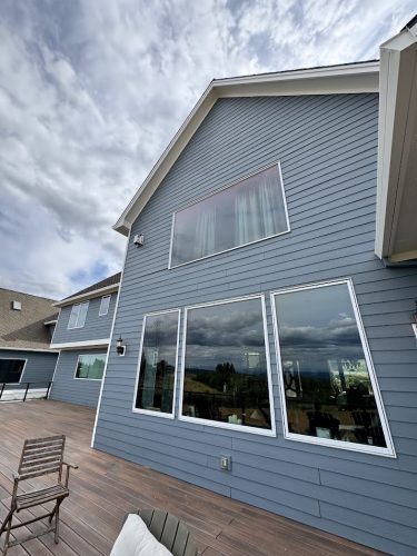 A modern Anderson house in Portland with blue siding and large windows, freshly painted by Pearl Painters, features a spacious wooden deck with outdoor seating under a cloudy June 2025 sky.