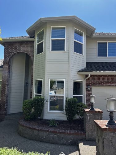 Pearl Painters, a Portland painter, will renovate the exterior of the two-story Mackey-Hinzdel house in June 2025. The painting project includes the brick and beige siding, bay window, arched entryway, and garden area with shrubs and stone lamps.