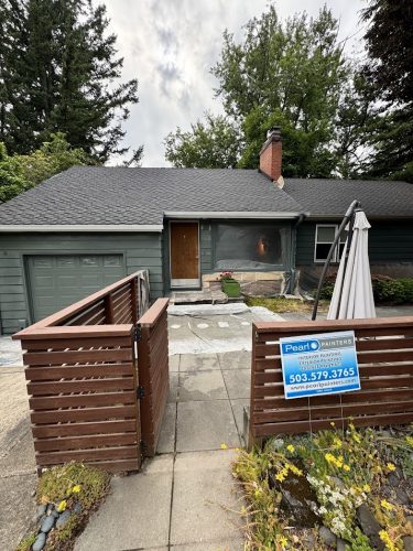 A single-story gray house in Carlton features a wooden fence, gate, concrete path, garage, and a Pearl Painters sign with contact information displayed out front. Photo taken June 2025.