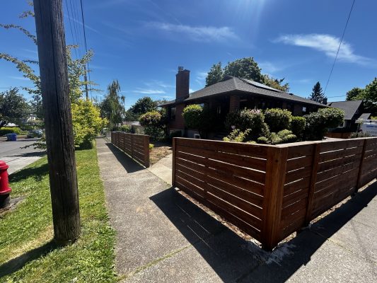 A painter from Pearl Painters observed a wooden fence around a brick house with a chimney in Trujillo on a sunny day in May 2025. This location is not Portland.