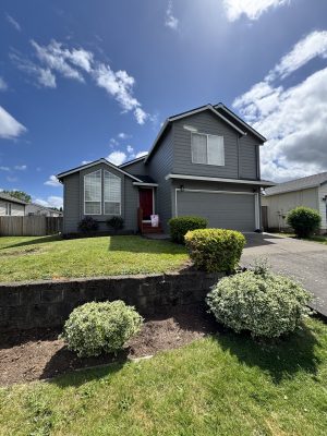A painter from Pearl Painters painted this two-story gray house with a red front door and attached garage in Portland. The painting was completed on a sunny day in May 2025.