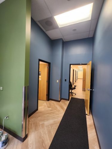 Pearl Painters, a Portland painter, completed a hallway painting at Jones Int in June 2025. The office features blue and green walls, a wood-patterned floor, wooden doors, a black runner rug, and ceiling lights.
