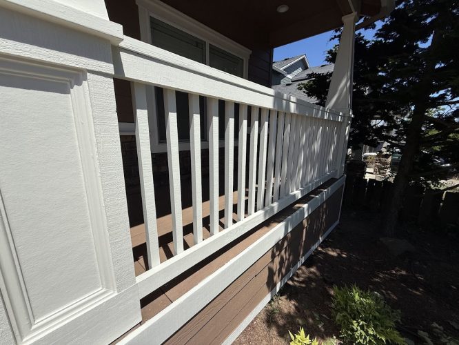 White wooden porch railing with brown trim, part of an Emory house, with greenery and trees in the background under a clear June 2025 sky. Painted by Pearl Painters, Portland painters.