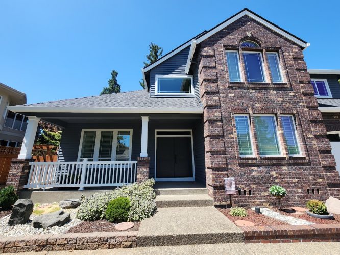 Two-story house with dark siding, brick, and white porch. Pearl Painters, Portland painter, painting exterior July 2025.