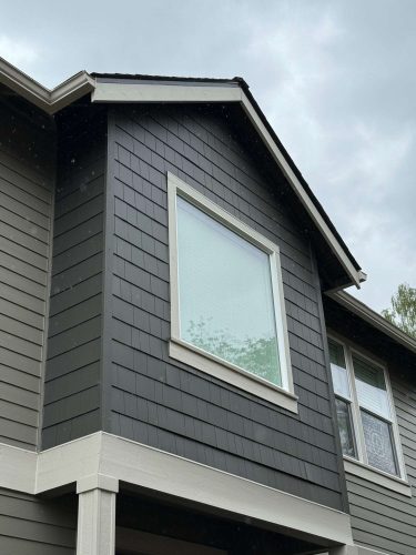 A painter from Pearl Painters completed the modern upper story of a house in Austin (not Portland) in May 2025, featuring dark gray siding, white trim, and two windows.