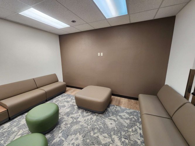 The Jones office waiting room in Portland features brown sofas, green ottomans, a large brown ottoman, a patterned rug, and beige and brown walls under fluorescent lights. Pearl Painters completed the update in May 2025.