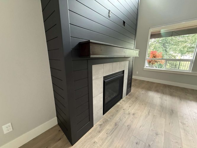Modern interior living room in Portland with a black shiplap fireplace, wood mantel, tiled surround, light wood floor, and large window. Painted by Pearl Painters.