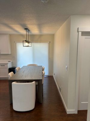 A painter from Pearl Painters in Portland painted this modern dining room, featuring a wooden table, six white chairs, a rectangular light fixture, and sliding glass doors with closed blinds.