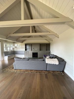 Spacious living room in Portland with vaulted ceiling, exposed beams, gray sectional, built-in shelves, fireplace, and large windows—showcasing timeless interior painting by Pearl Painters.