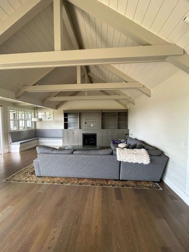 Spacious living room in Portland with vaulted ceiling, exposed beams, gray sectional, built-in shelves, fireplace, and large windows—showcasing timeless interior painting by Pearl Painters.