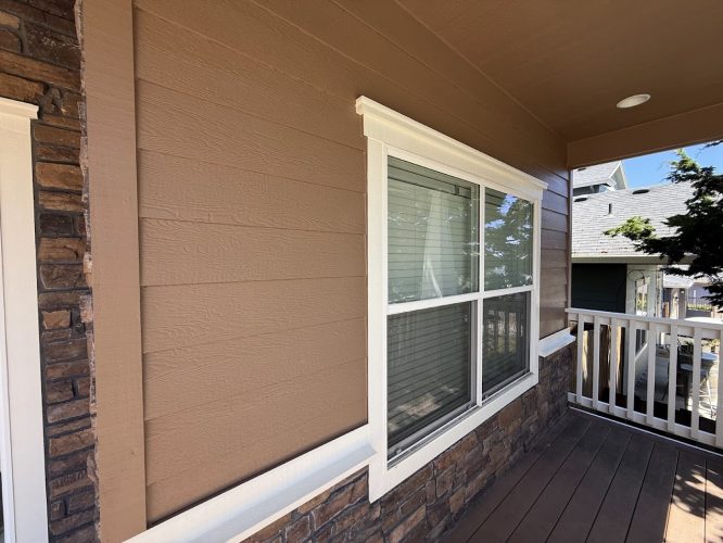 Close-up of an Emory house exterior in Portland with brown siding, white-trimmed window, stone accents, and wooden porch railing, painted by Pearl Painters in June 2025.