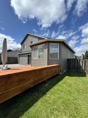 A two-story gray house with white trim—recently painted by Pearl Painters—features a stylish exterior and sits behind a raised wooden deck in a fenced backyard in Portland.