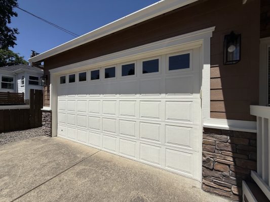 Pearl Painters painted a white double garage door with rectangular windows at the top on a brown Emory house with stone trim in Portland, next to a concrete driveway, June 2025.
