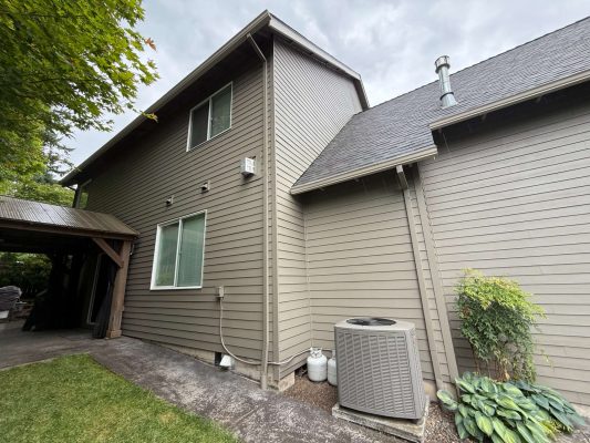 Exterior view of a two-story gray house in Austin, with large windows, covered patio, AC unit, and propane tanks; not painted by Portland’s Pearl Painters.