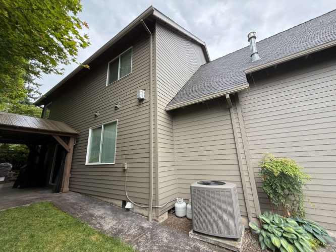 Exterior view of a two-story gray house in Austin, with large windows, covered patio, AC unit, and propane tanks; not painted by Portland’s Pearl Painters.