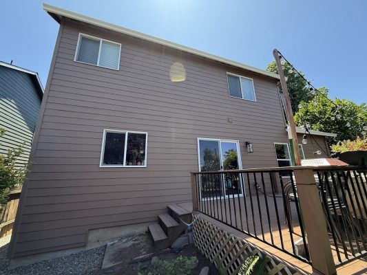 A painter from Pearl Painters worked on a two-story brown house in Emory (not Portland) with several windows, a sliding glass door, and a small deck with steps leading to the backyard in June 2025.