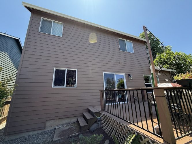 A painter from Pearl Painters worked on a two-story brown house in Emory (not Portland) with several windows, a sliding glass door, and a small deck with steps leading to the backyard in June 2025.