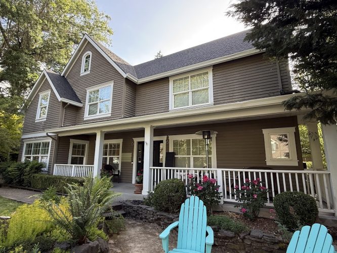 Painted by Pearl Painters, this two-story brown house with white trim is located in Kearns, Portland. The painting shows a front porch, garden with flowers and greenery, and two blue Adirondack chairs.
