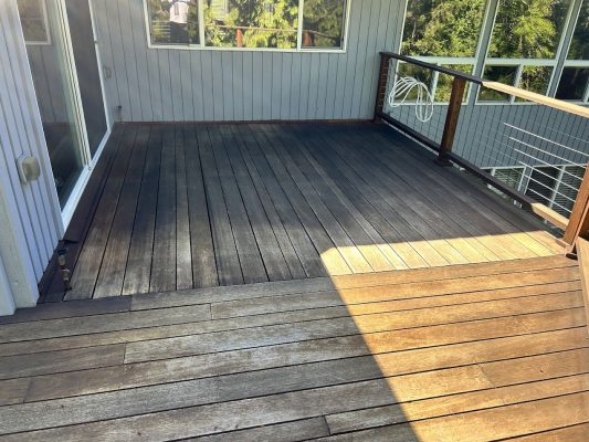 A Shainsky wooden deck with sun and shade, wire railing, and glass doors is attached to a gray-sided house in Portland. Pearl Painters can prepare your deck for relaxing moments by June 2025.