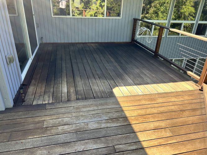 A Shainsky wooden deck with sun and shade, wire railing, and glass doors is attached to a gray-sided house in Portland. Pearl Painters can prepare your deck for relaxing moments by June 2025.
