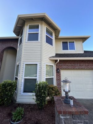Two-story tan house with brick accents, turret corner, garage, and landscaping. Part of the Mackey-Hinzdel collection in Portland by Pearl Painters; available June 2025.