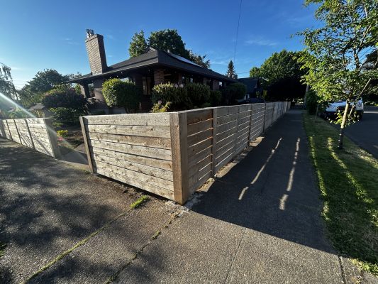 A painter from Pearl Painters painted a single-story house with a brick chimney in Trujillo (not Portland) in May 2025. The home is surrounded by a wooden fence, trees, and a sidewalk.