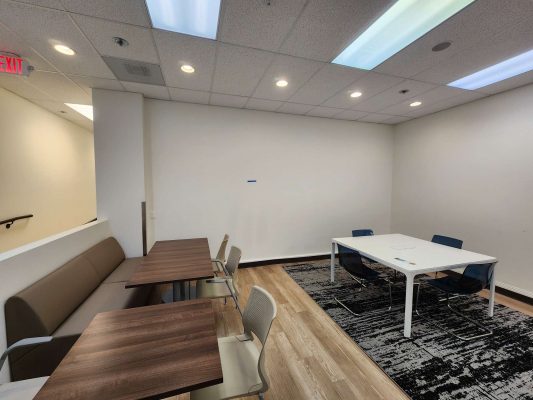 The Jones office in Portland features wooden tables and chairs on the left, a white table with blue chairs on a rug to the right, and overhead lights. Pearl Painters completed the painting.