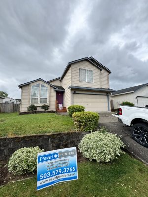 A Pearl Painters sign offering exterior painting services is in front of a two-story beige house with a manicured lawn in Portland. Offer valid through May 2025.
