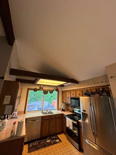 This kitchen in Oneal features wooden cabinets, stainless steel appliances, a window over the sink, exposed beams, and hanging pots. Pearl Painters is a Portland painting company available for your May 2025 home refresh.