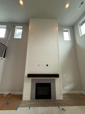 A tall, white shiplap fireplace with a dark wood mantel and black-framed firebox is being painted by Pearl Painters in this modern Portland living room, designed by Turk and set for May 2025 completion.