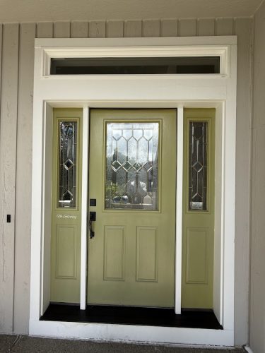 A green front door with decorative glass panels and sidelights, framed by beige siding and white trim, is a painting idea for your Hendricks home. For professional painters in Portland, contact Pearl Painters.