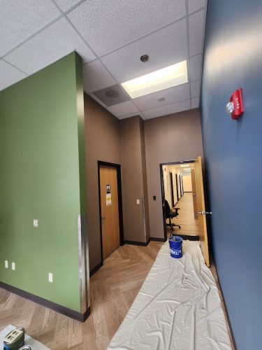 Paint supplies are ready on the floor of a Portland hallway with brown doors, blue, green, and beige walls. Pearl Painters will begin painting here in June 2025.