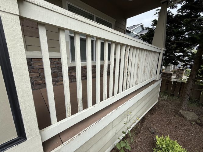 A white wooden porch railing with peeling paint and weathering is attached to a beige house with stone accents in Emory. The condition indicates the need for painting by a professional painter, such as Pearl Painters of Portland. Photo taken June 2025.