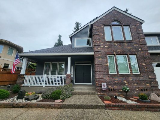 Roberts' two-story brick house in Portland, freshly painted by Pearl Painters, with porch, double doors, and flag.