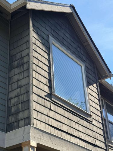 Close-up of the upper story of a house in Austin, showing gray wood shingles and a large rectangular window under a blue May 2025 sky. No work by Pearl Painters or any Portland painter is depicted; this is not a Portland painting.